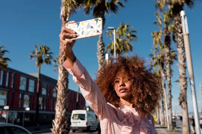 Stylish young woman taking a selfie at seaside promenade