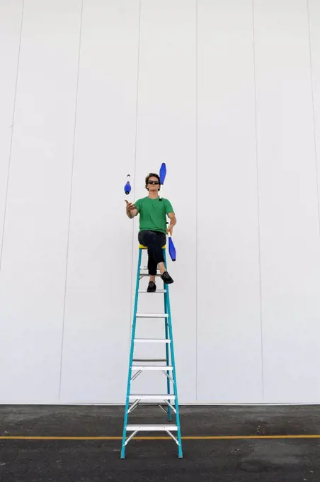 Acrobat wearing sunglasses, sitting on ladder, juggling
