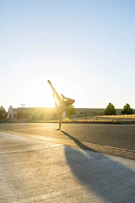 Acrobat practicing one-armed handstand on a road at sunset