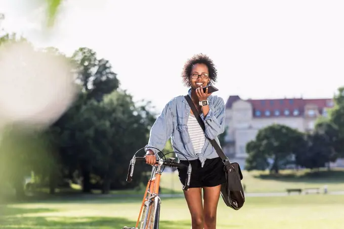 Smiling young woman with cell phone and bicycle in park