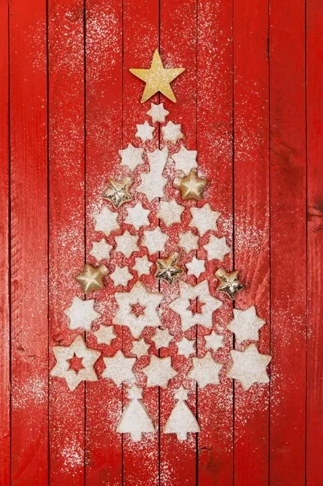 Christmas cookies and star-shaped Christmas baubles forming Christmas tree on red wooden background