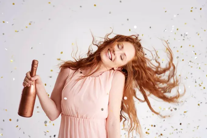 Portrait of happy young woman dancing with bottle of champagne