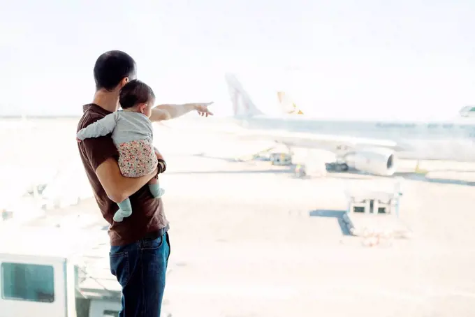 Spain, Barcelona, Man holding a baby girl at the airport pointing at the airplanes