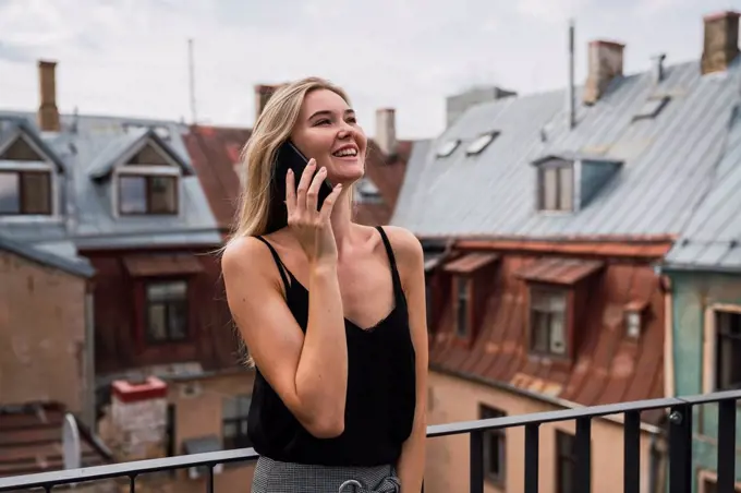 Smiling blond woman on the phone standing on balcony looking up