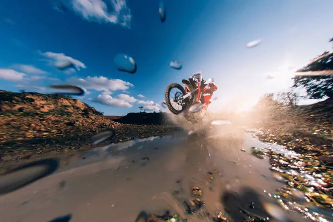 Motocross driver driving through the water, splashing