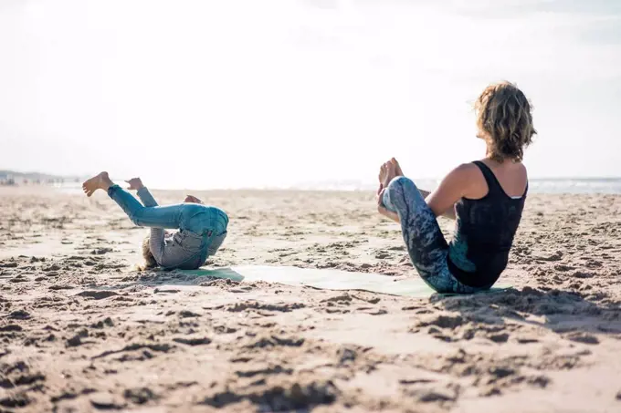 Mother and daughter practising yoga on the beach