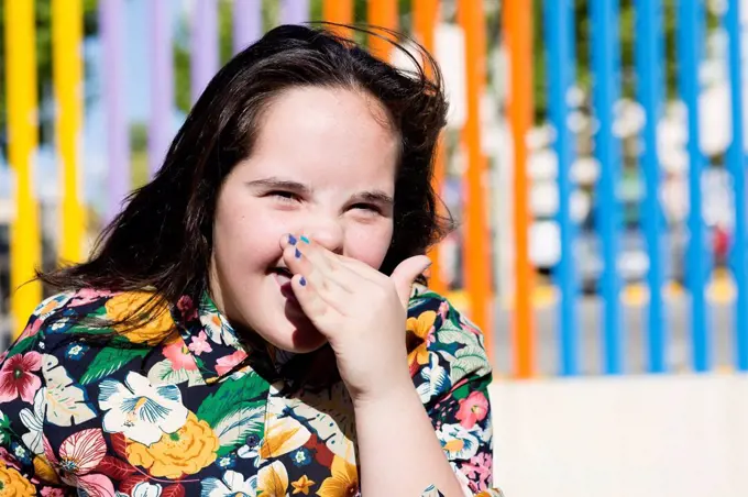 Teenager girl with down syndrome laughing, hand covering mouth