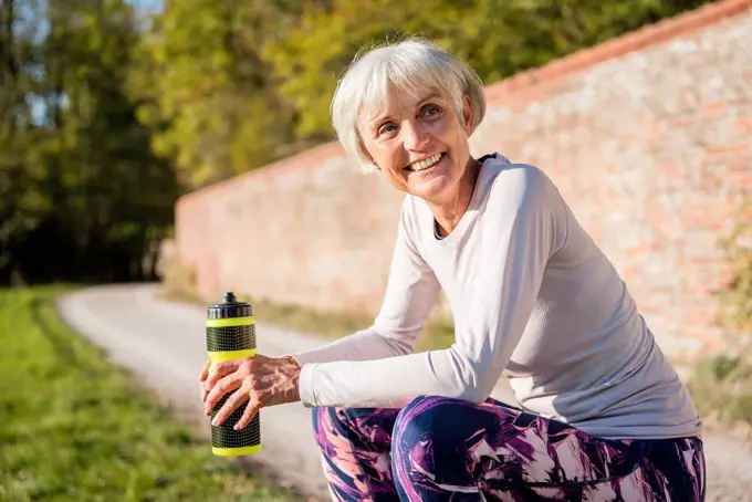 Smiling sportive senior woman holding bottle in park