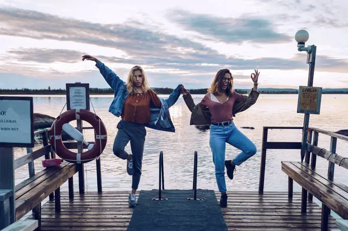 Two girl friends standing on one leg on a pier at Lake INari, Finland