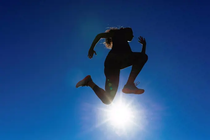 Sportive young woman jumping under blue sky in backlight
