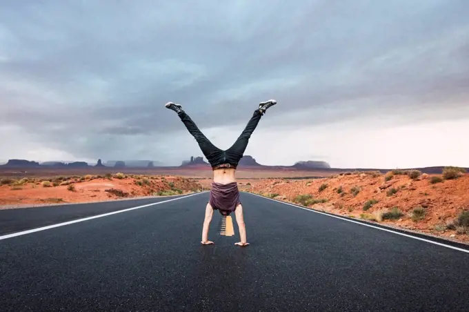 USA, Utah, Young man dong handstand on road to Monument Valley