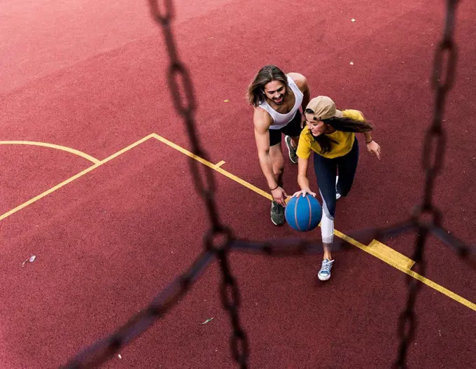 Young man and woman playing basketball on basketball ground
