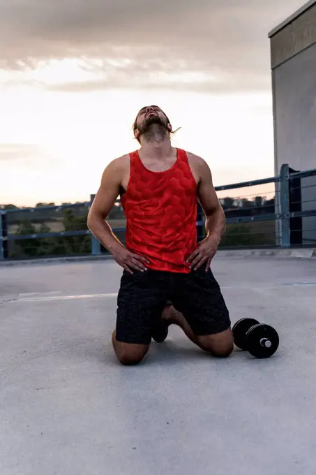 Exhausted athlete kneeling on ground after workout