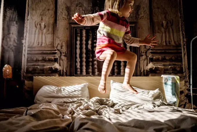 Little girl jumping on parent's bed at home