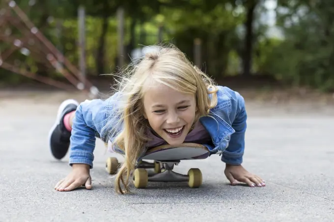 Portrait of laughing blond girl lying on her skateboard outdoors