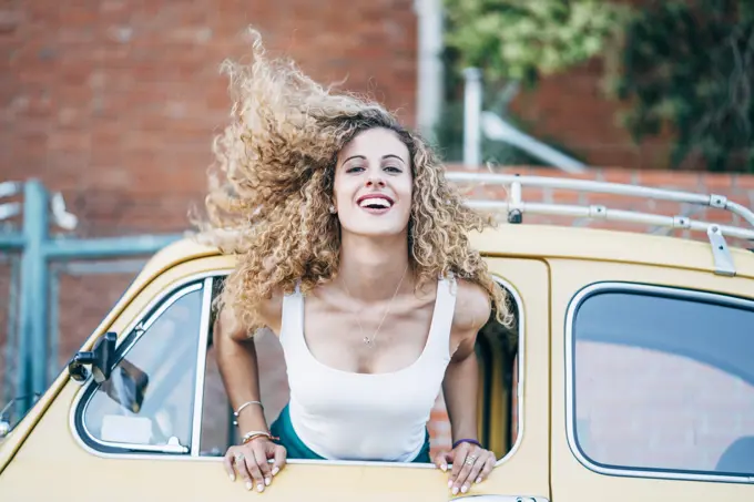 Portrait of blond woman leaning out of window of classic car tossing her hair