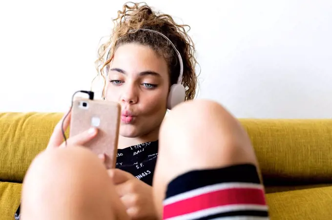 Portrait of whistling girl sitting on the couch listening music with headphones and smartphone