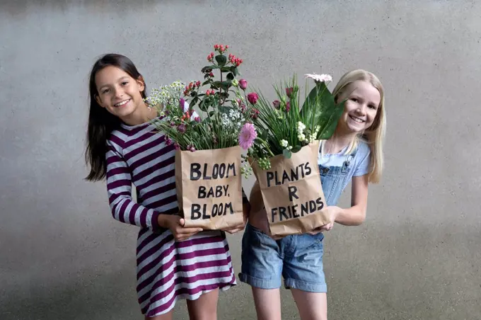 Portrait of two smiling girls holding paper bags with flowers