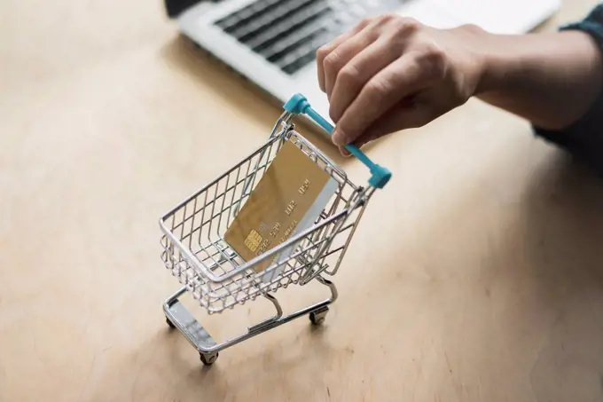 Woman's hand holding mini shopping cart with credit card