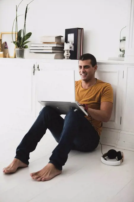 Smiling young man sitting on the floor using laptop
