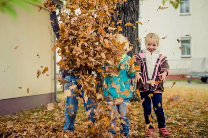 Three children throwing autumn leaves