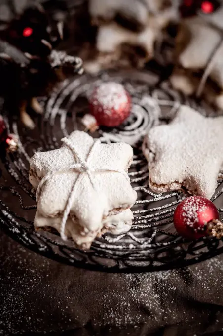 With powdered sugar sprinkled star-shaped cinnamon cookies and red Christmas baubles on cake stand