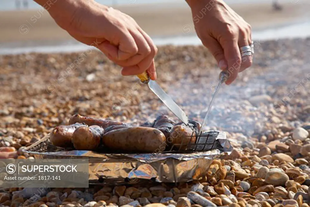 Young person barbequing sausages on the beach 