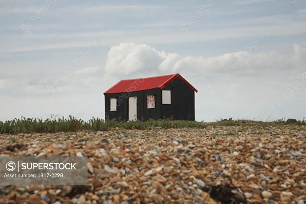 Rustic red roofed beach hut with Union Jack shutter in England
