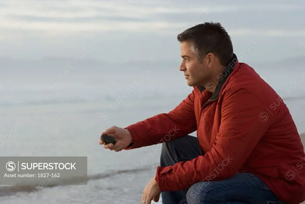 Side profile of a mid adult man holding a stone on the beach