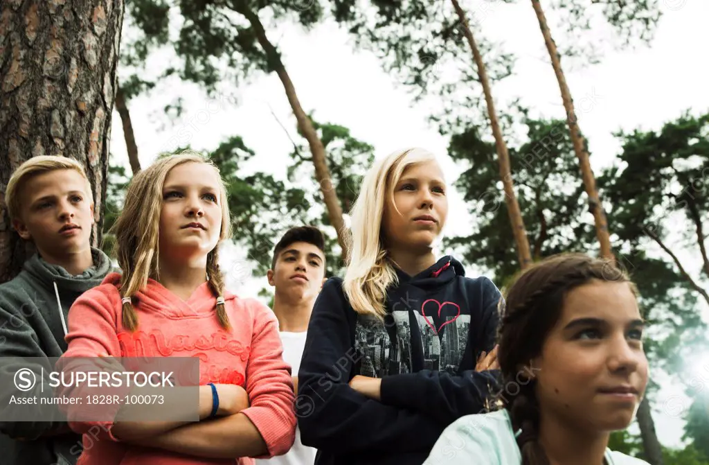 Portrait of group of children standing next to trees in park with arms crossed, looking forward in same direction, Germany. 08/31/2013