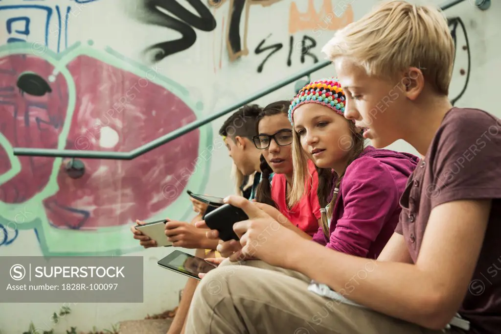 Group of children sitting on stairs outdoors, using tablet computers and smartphones, Germany. 08/31/2013