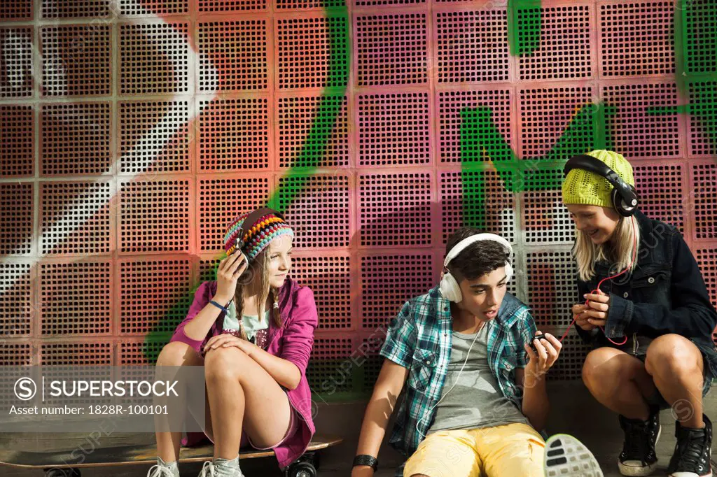 Children sitting next to wall outdoors, wearing headphones and listening to music, Germany. 08/31/2013