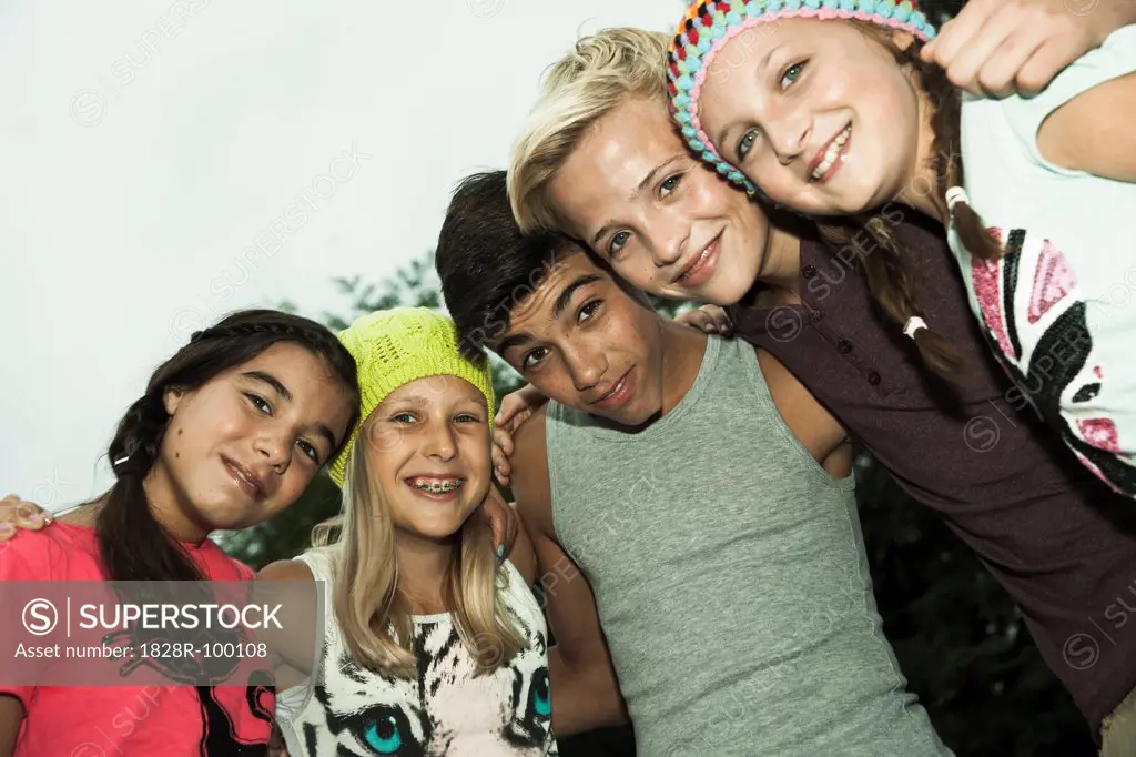 Group of children standing together with arms around eath other, looking down and smiling at camera, Germany. 08/31/2013