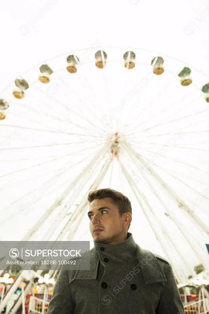 Portrait of young man standing in front of ferris wheel at amusement park, Germany. 10/12/2013