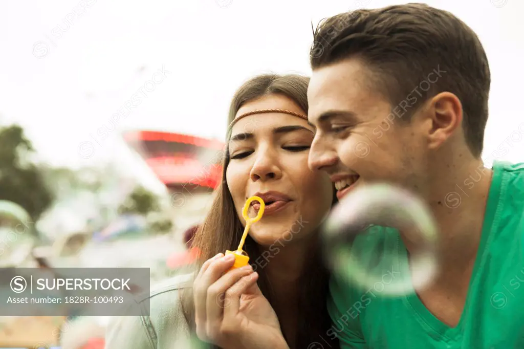 Close-up portrait of young couple blowing bubbles at amusement park, GermanyYoung. 10/12/2013