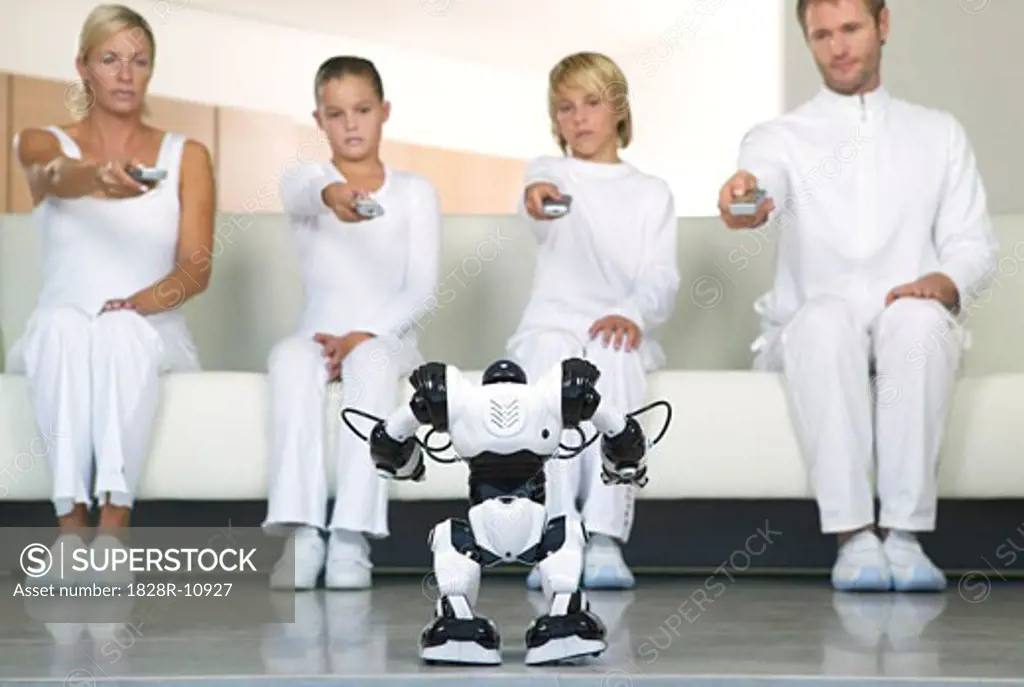 Portrait of Family Sitting on Sofa, Using Remote Controls on Robot   