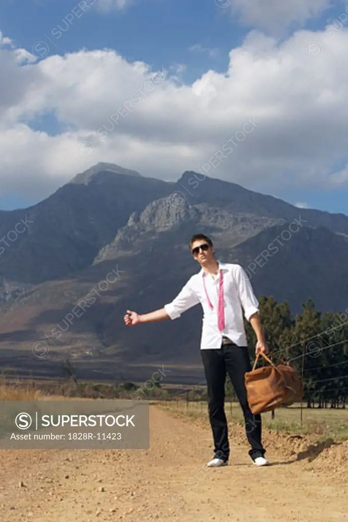 Young Man Hitchhiking On Country Road   
