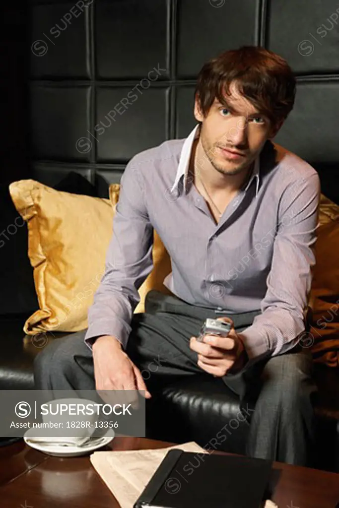 Businessman in Hotel Lobby with Cellular Phone and Coffee   