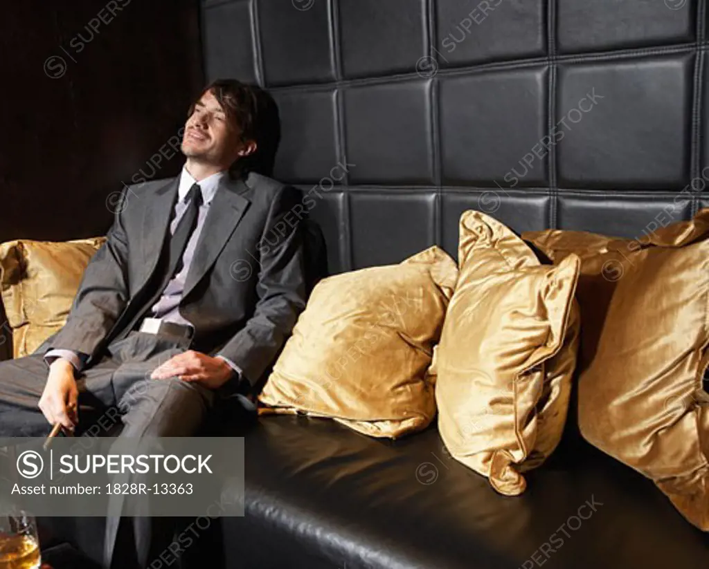 Man Relaxing on Sofa with Cigar and Liquor   