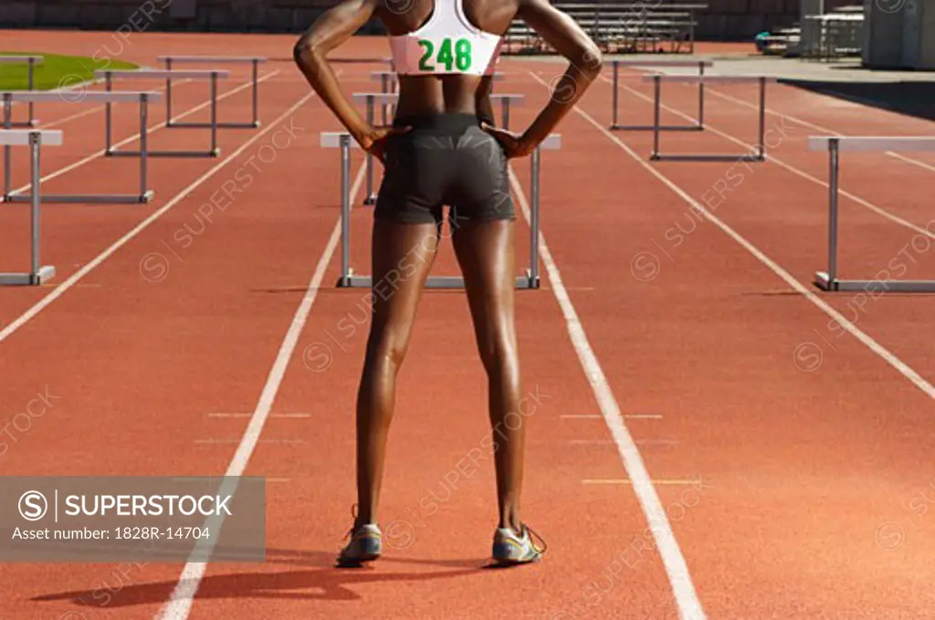 Back View of Woman Standing in Front of Hurdles on Track   