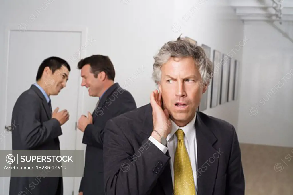 Businessman Listening to Colleagues Gossiping in Hallway   