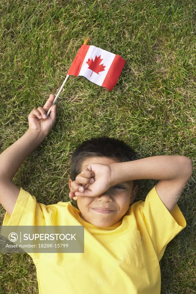 Portrait of Boy Lying on Grass, Holding Canadian Flag   