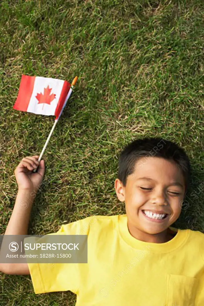Portrait of Boy Lying on Grass, Holding Canadian Flag   