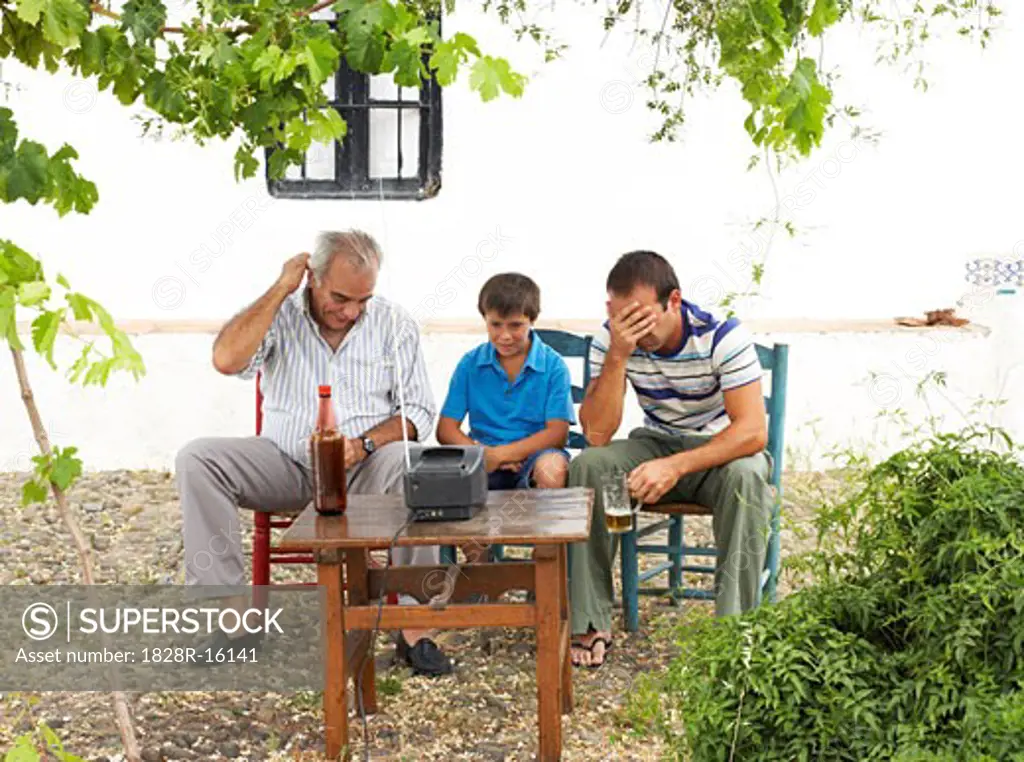 Grandfather, Father and Son Watching Television in Backyard   