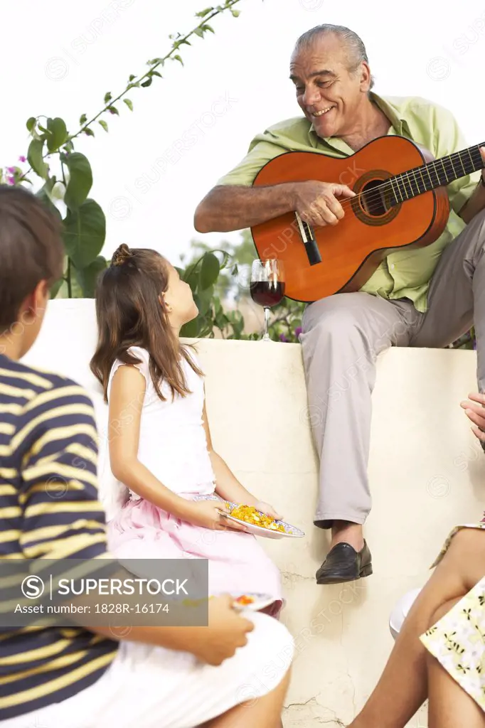 Man Playing Guitar Outdoors with Children Listening   