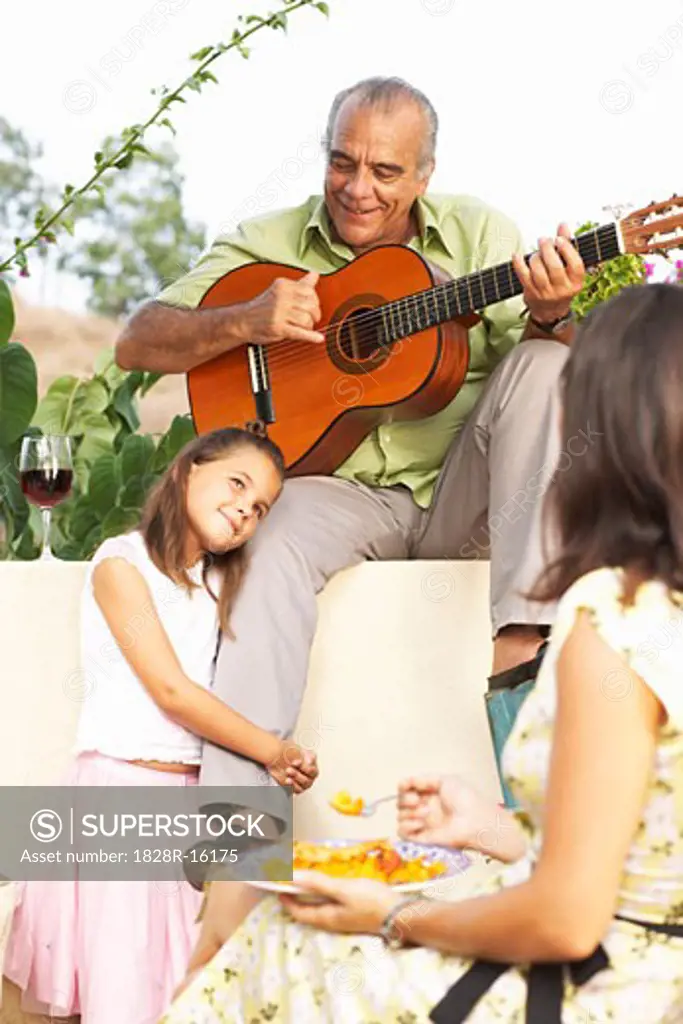 Man Playing Guitar Outdoors and Child Holding onto his Leg   