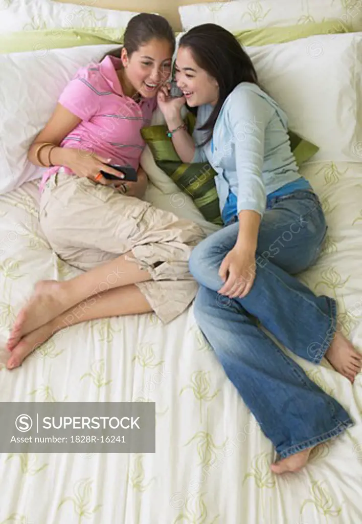 Friends Using Cellular Phones on Bed   