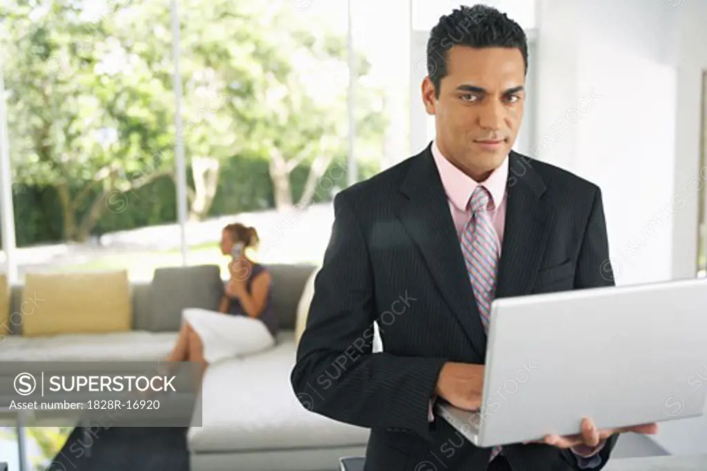 Businessman Holding Laptop, Woman in Background   