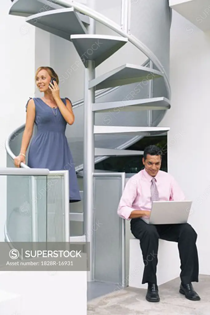 Couple at Staircase Using Cellular Phone and Laptop   