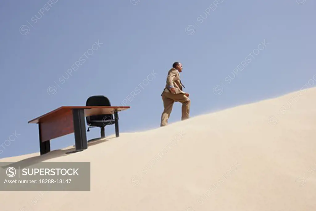 Businessman Walking away from Office on Sand Dune   